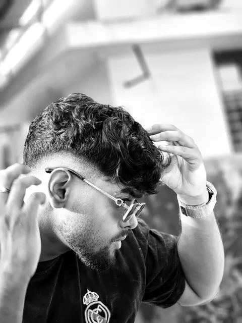 Black and white portrait of a man in glasses running both hands through his hair, a building soft behind him.